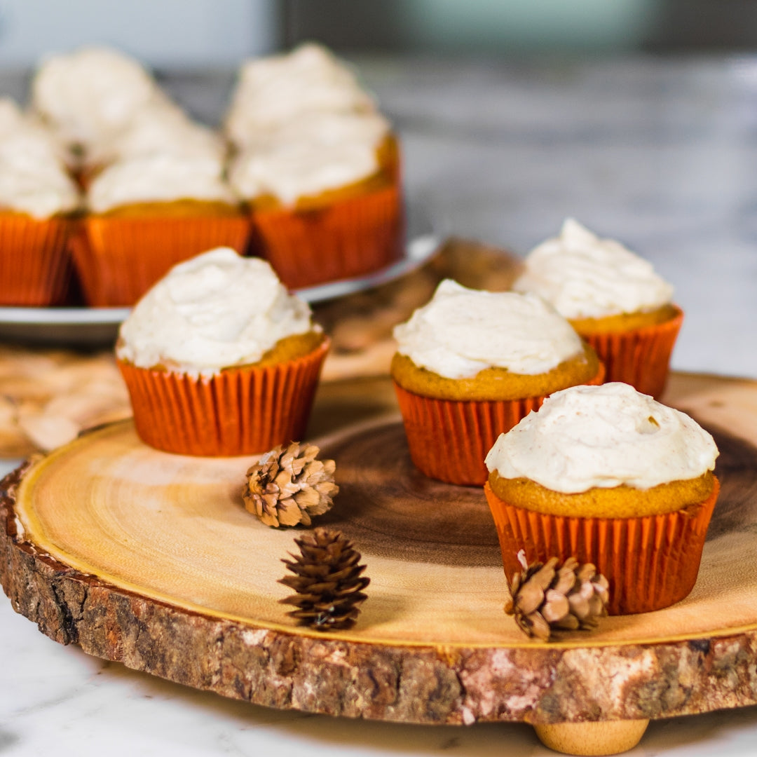 Pasolivo Pumpkin Cupcakes with Sugar & Spice Cream Cheese Frosting Recipe on a table next to pinecone decorations
