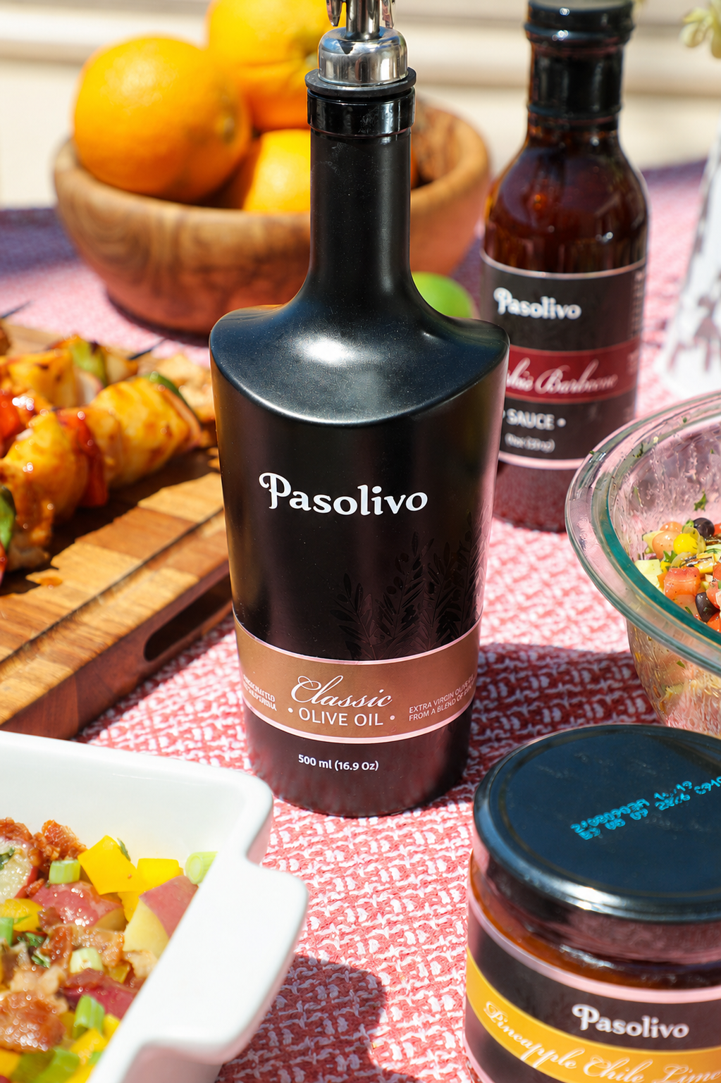 Bottles of Pasolivo extra virgin olive oil and sauce on a table with food in the background