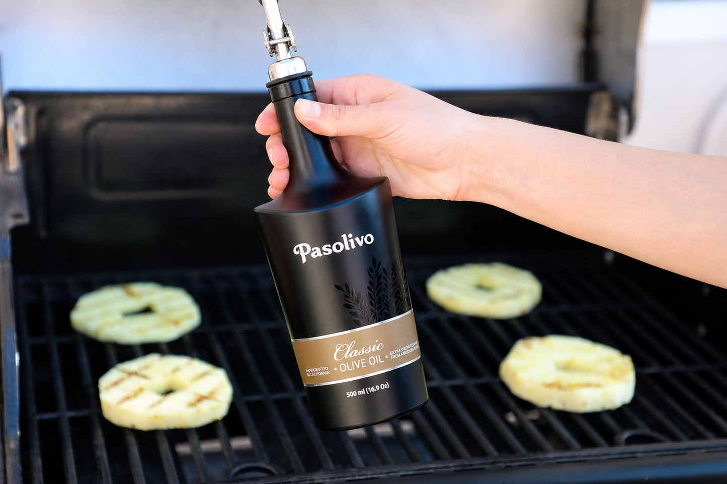 Person using a Pasolivo Classic extra virgin olive oil bottle on a grill with food in the background