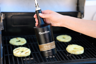 Person using a Pasolivo Classic extra virgin olive oil bottle on a grill with food in the background