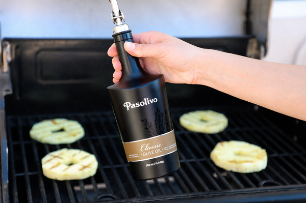 Person using a Pasolivo Classic extra virgin olive oil bottle on a grill with food in the background