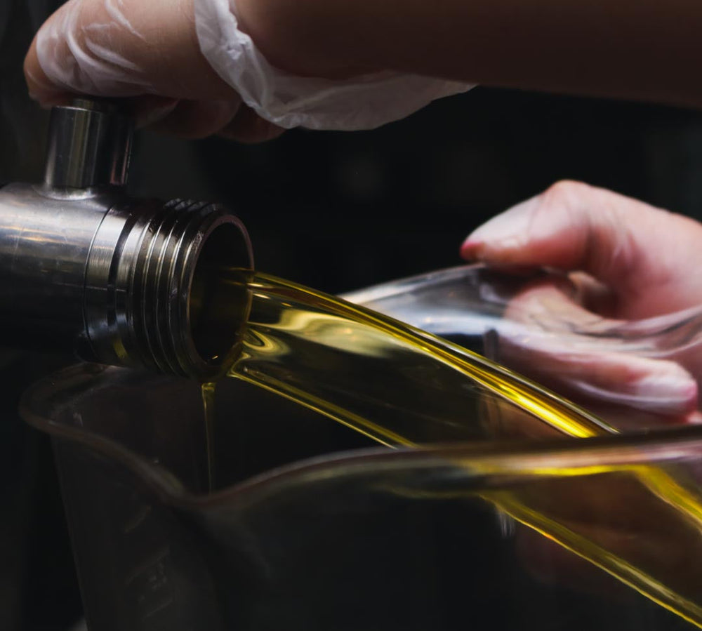 Person pouring yellow liquid from a metal container into a glass container.