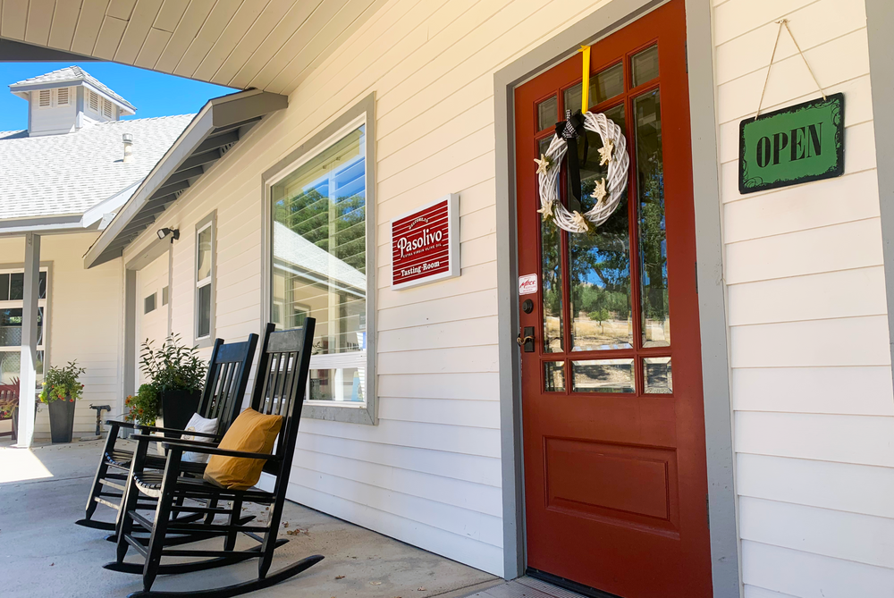 Front porch of a house with rocking chairs, a wreath on the door, and an 'Open' sign.