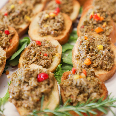 Platter of appetizers with crostini topped with green olive tapenade and garnished with herbs.