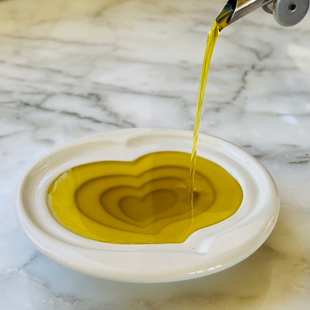Olive oil being poured into a heart-shaped dish on a marble surface