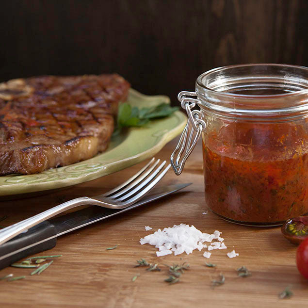 Pasolivo California Blend Olive Oil Marinade Recipe in a clear jar resting on wooden countertop next to plated steak