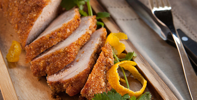 Pasolivo Pork Tenderloin Recipe garnished with tangerine peels and herbs next to silverware