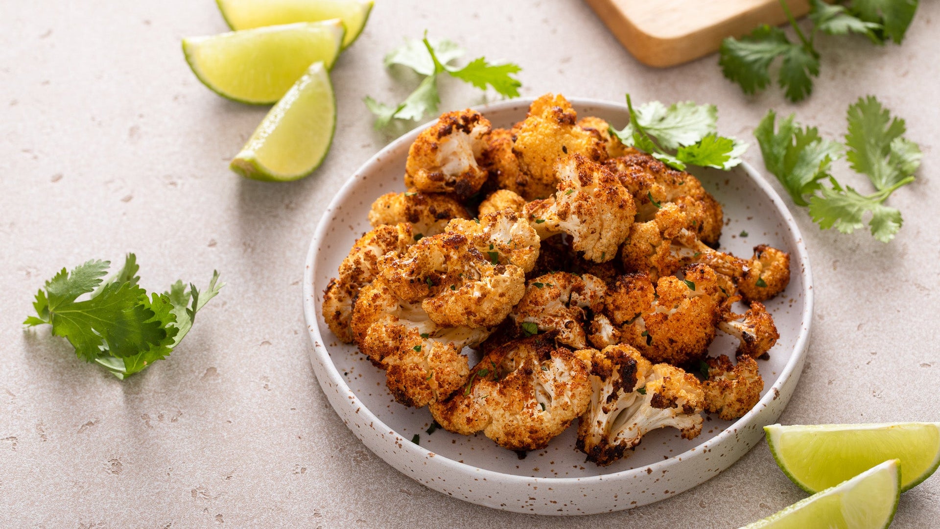Plated roasted cauliflower with lime wedges and cilantro on a light surface