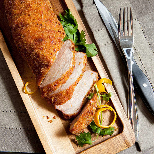 Pasolivo Pork Tenderloin Recipe garnished with tangerine peels and herbs next to silverware